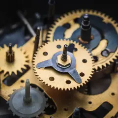 Złote i metalowe trybiki tworzą skomplikowany mechanizm zegara ściennego, pracujący w harmonii, by odmierzać czas.