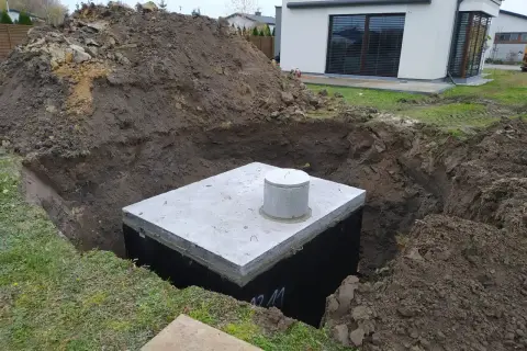 Betonowy zbiornik na deszczówkę w wykopie, otoczony ziemią.