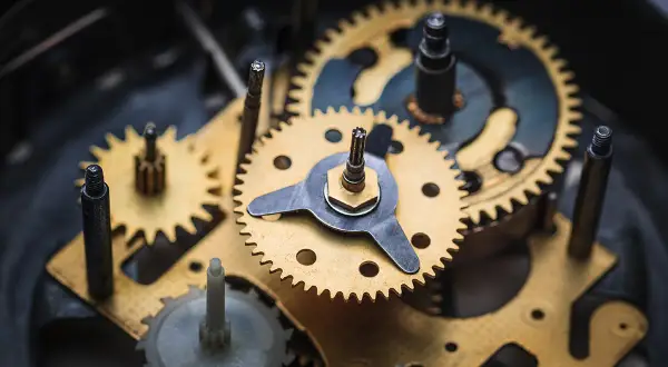 Złote i metalowe trybiki tworzą skomplikowany mechanizm zegara ściennego, pracujący w harmonii, by odmierzać czas.