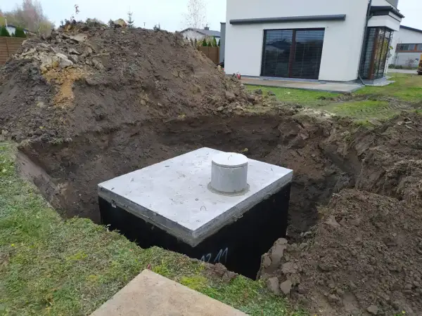 Betonowy zbiornik na deszczówkę w wykopie, otoczony ziemią.